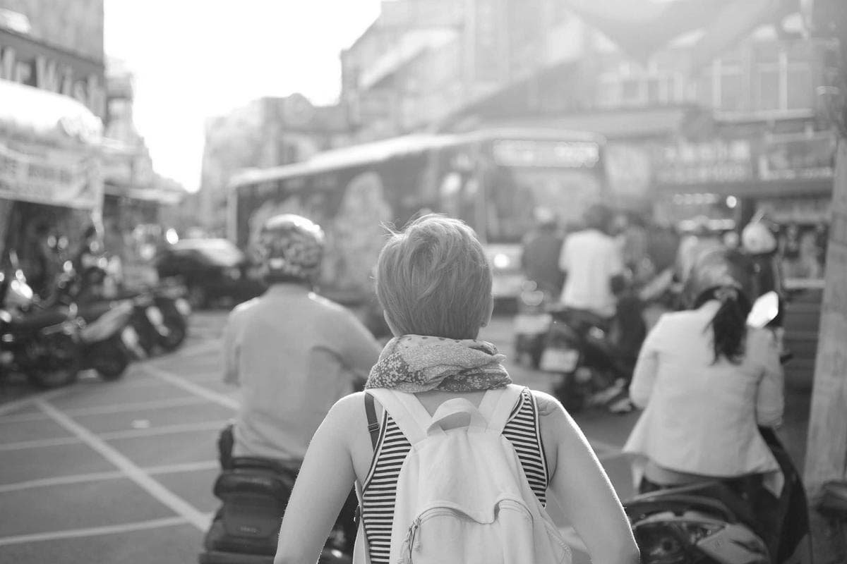 A busy street scene with pedestrians and mopeds in motion, captured in grainy black and white with visible motion blur.