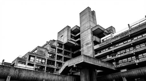A high-contrast black and white photograph of a brutalist architecture structure against a stark white sky, emphasizing geometric lines and raw textures, representing modern cultural foundations.