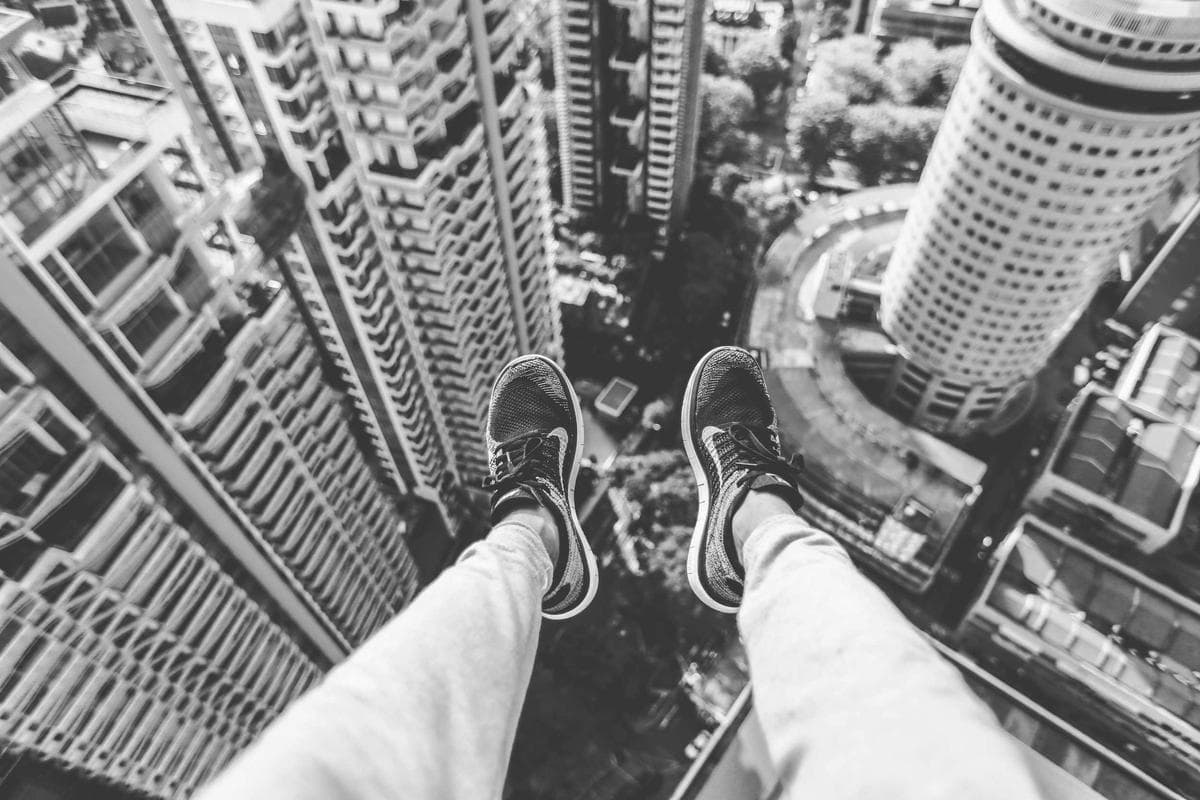 A point-of-view shot looking straight down between two skyscrapers, with a person's shoes visible at the edge of the frame.