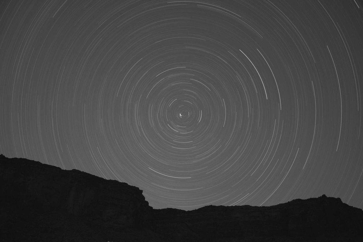 A long-exposure night photograph showing circular star trails above a dark mountain ridge.