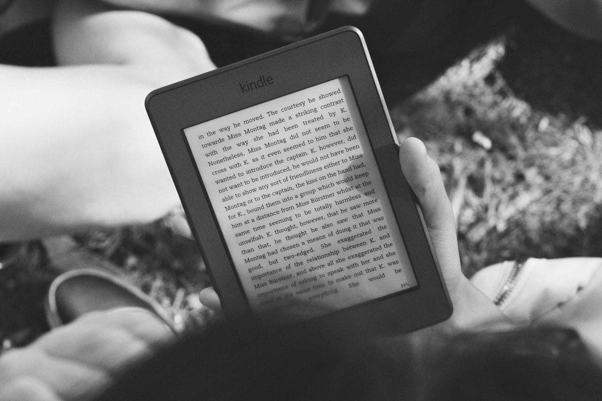 A close-up of a hand holding a small e-reader device displaying a page of text.