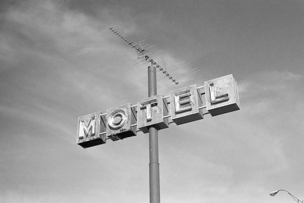 A vintage illuminated motel sign with large block letters, photographed against a plain sky.