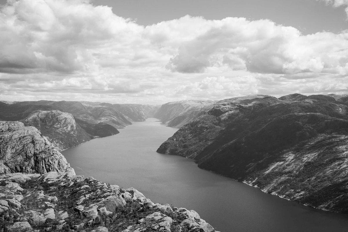 An aerial view of a winding river cutting through a mountainous valley, photographed in black and white.