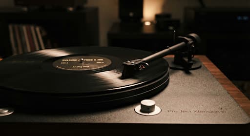 A dimly lit, moody photograph of a vintage vinyl record spinning on a high-end turntable, with a minimalist dark grey aesthetic and sharp focus on the stylus.